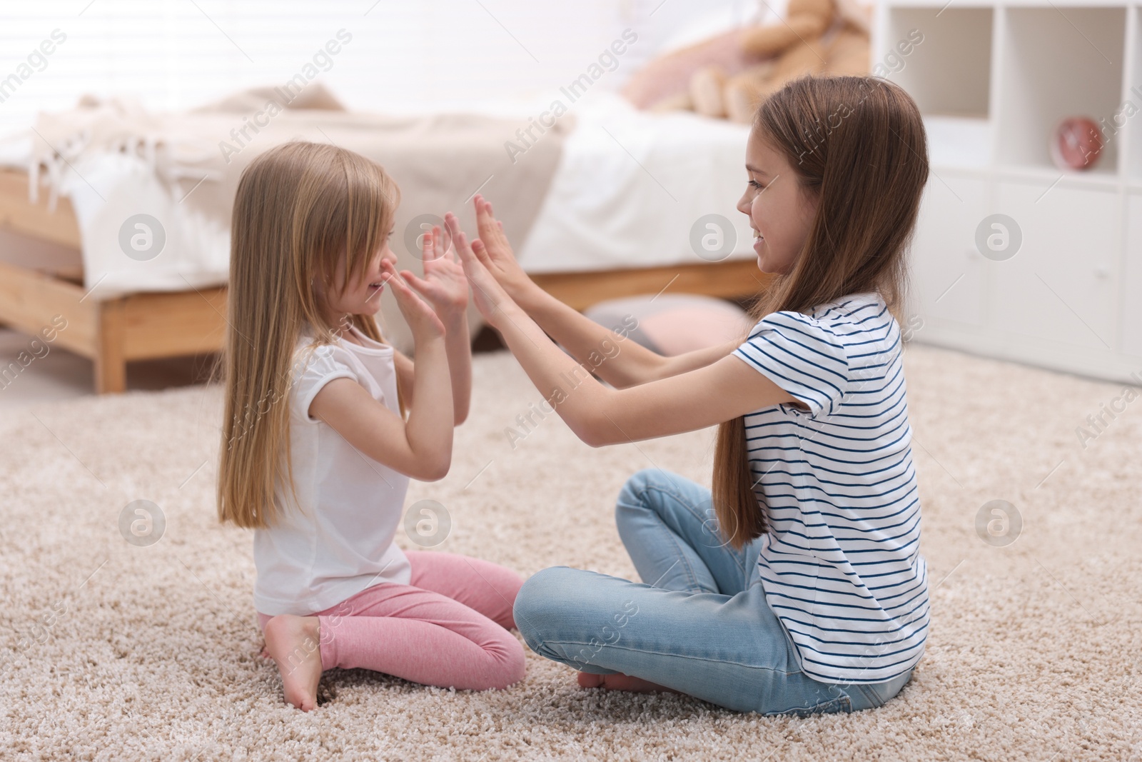 Photo of Cute little sisters playing clapping game with hands at home