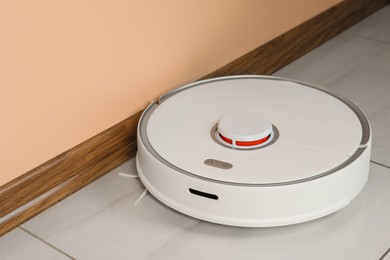 Photo of Robotic vacuum cleaner on white tiled floor near beige wall