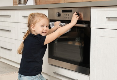 Photo of Little girl baking cookies in oven at home