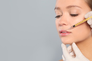 Photo of Young woman getting lips injection on grey background, space for text. Cosmetic surgery
