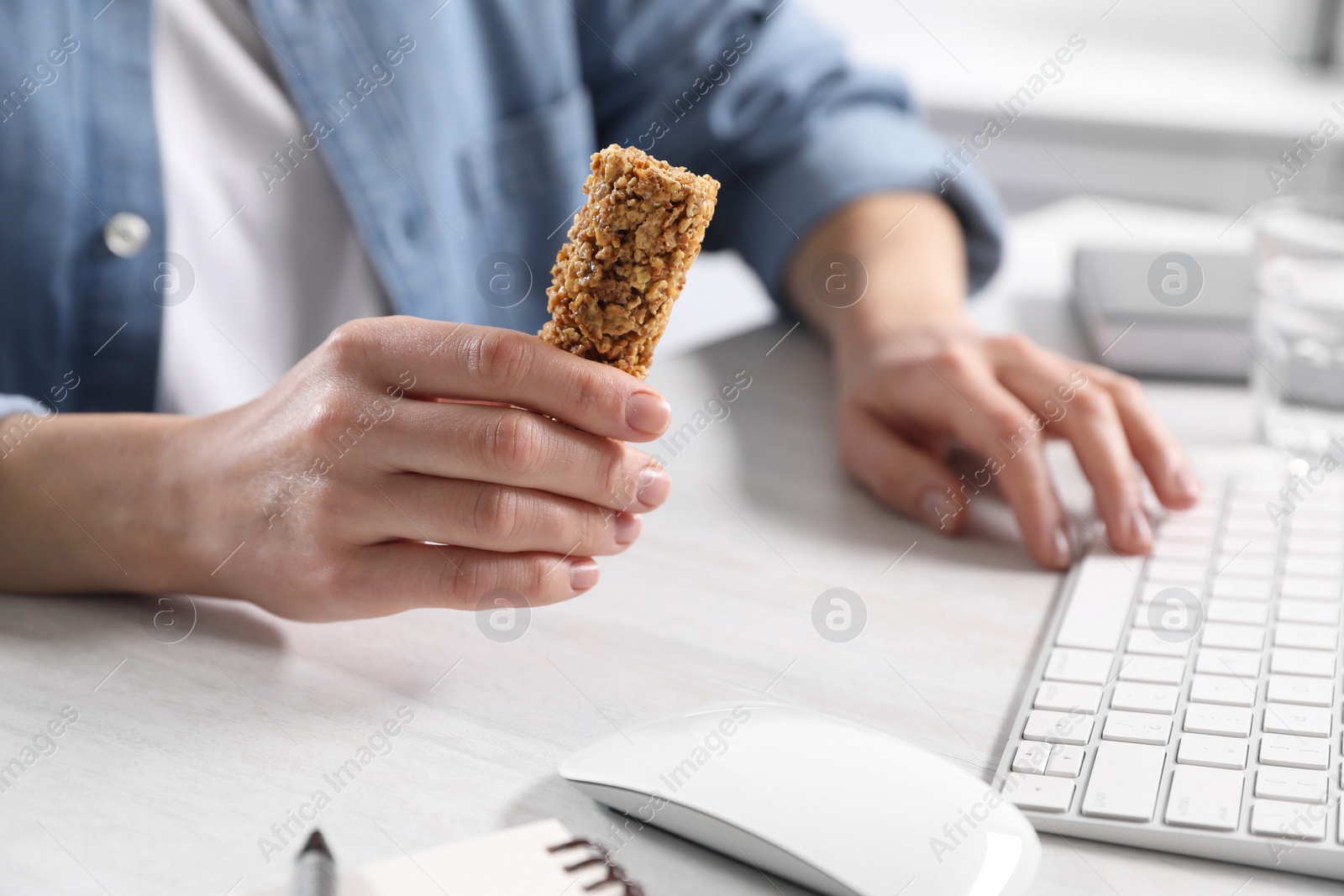 Photo of Woman holding tasty granola bar working with computer at light table in office, closeup