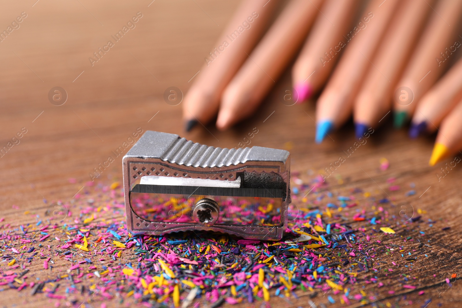 Photo of Metal sharpener, colorful graphite crumbs and pencils on brown wooden table, closeup