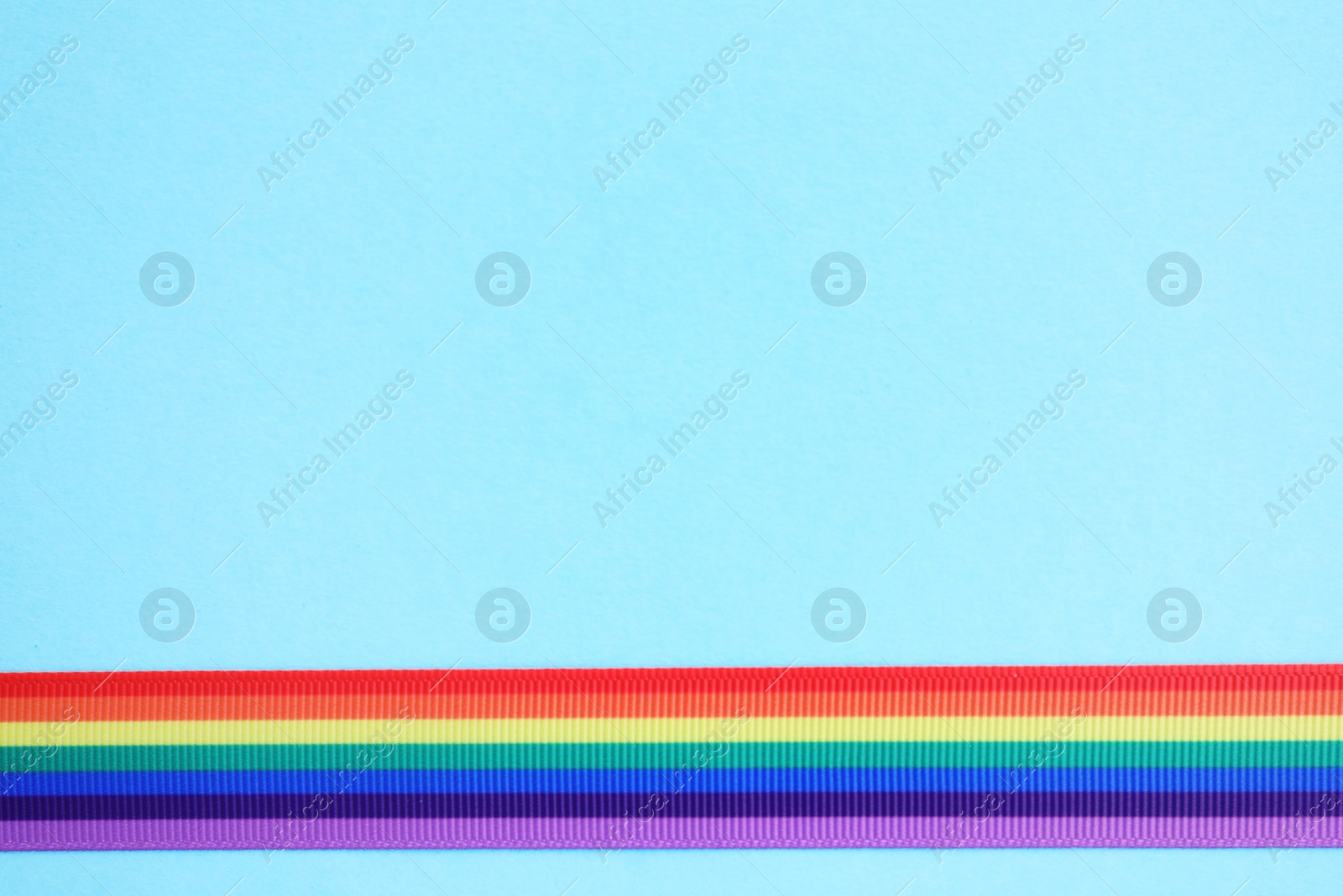 Photo of Bright rainbow ribbon on color background, top view with space for text. Symbol of gay community