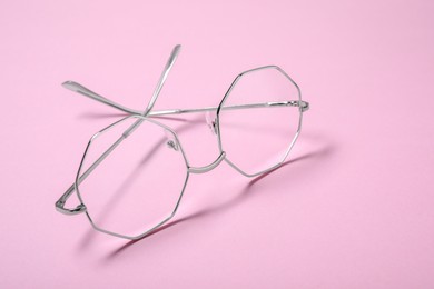 Stylish pair of glasses with metal frame on pink background, closeup