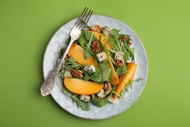 Photo of Tasty salad with persimmon, blue cheese and walnuts served on light green background, top view