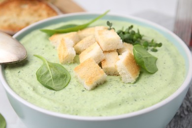 Delicious spinach cream soup with croutons in bowl on white table, closeup