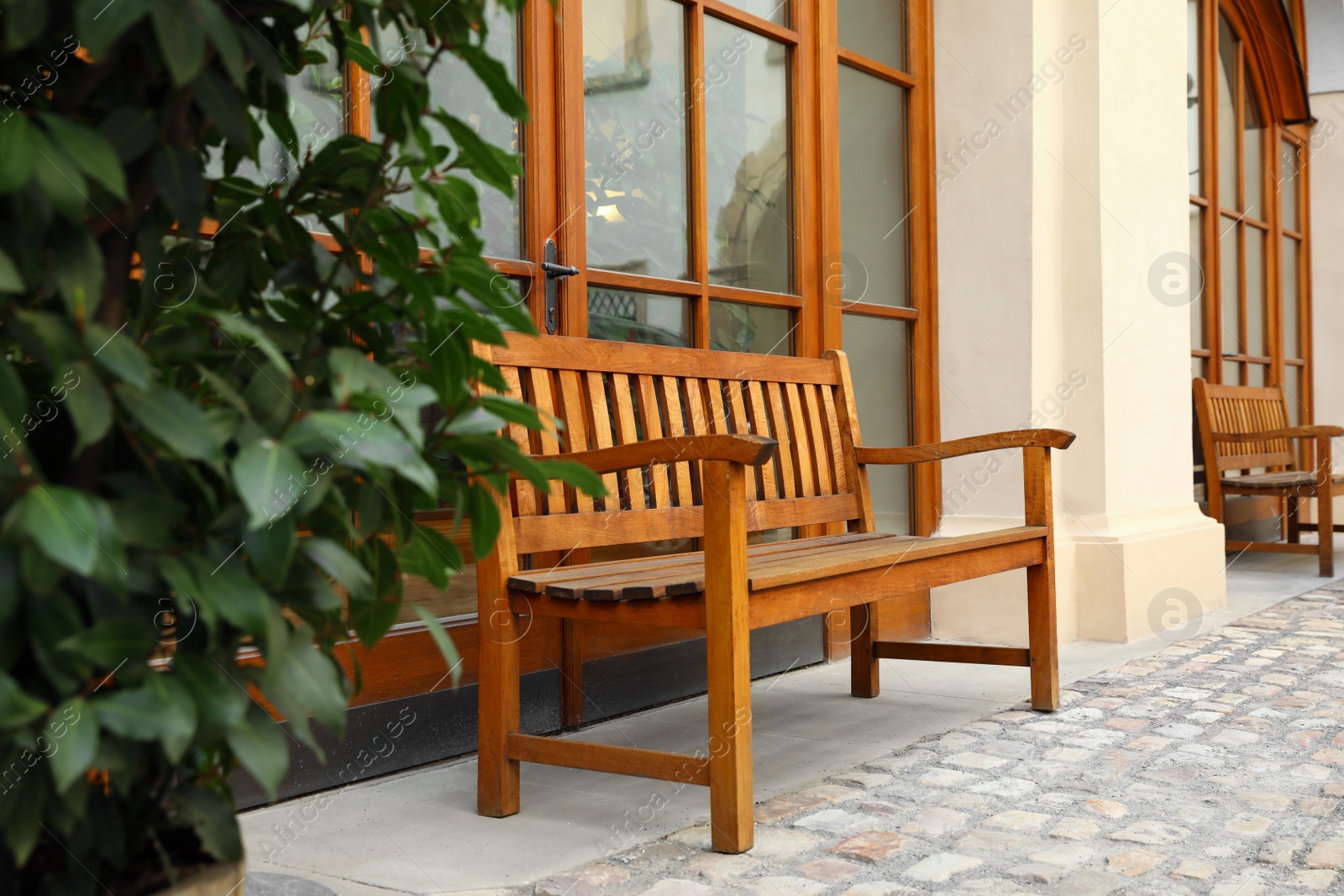 Photo of Comfortable wooden bench near building and green bush outdoors