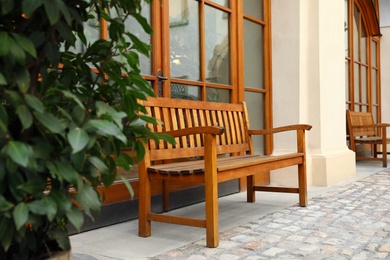 Comfortable wooden bench near building and green bush outdoors