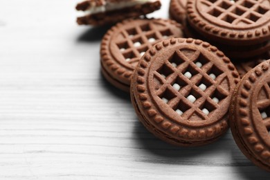 Photo of Tasty chocolate sandwich cookies with cream on white wooden table, closeup. Space for text