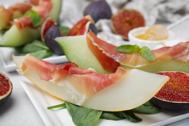 Photo of Tasty melon, jamon and figs served on white plate, closeup