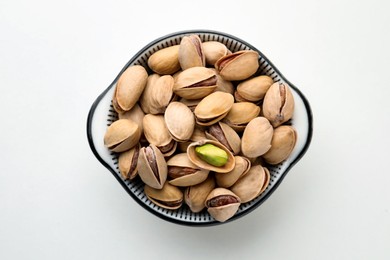 Bowl with pistachio nuts on white background, top view