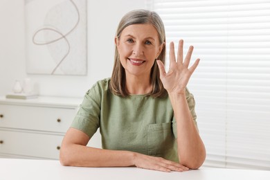 Photo of Happy woman waving hello at white table indoors