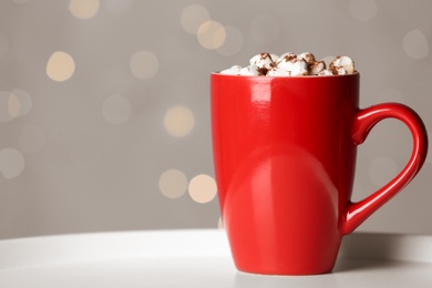 Cup of tasty cocoa with marshmallows on white table against blurred lights. Space for text