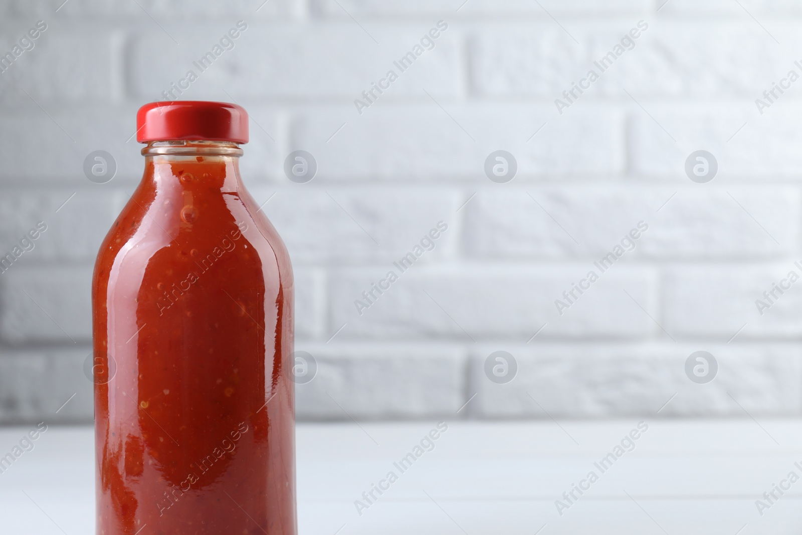 Photo of Spicy chili sauce in bottle on white wooden table, space for text