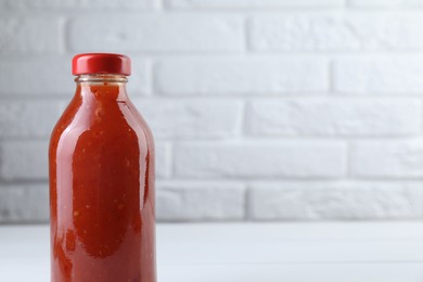 Photo of Spicy chili sauce in bottle on white wooden table, space for text