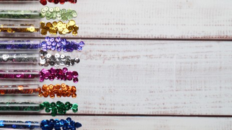 Photo of Tubes with many colorful sequins on white wooden table, flat lay. Space for text