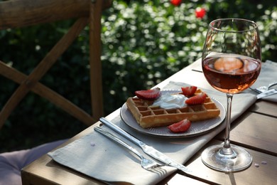 Photo of Delicious Belgian waffle with fresh strawberries and wine served on table in spring garden