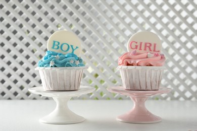 Photo of Delicious cupcakes decorated with Girl and Boy toppers for baby shower on white table
