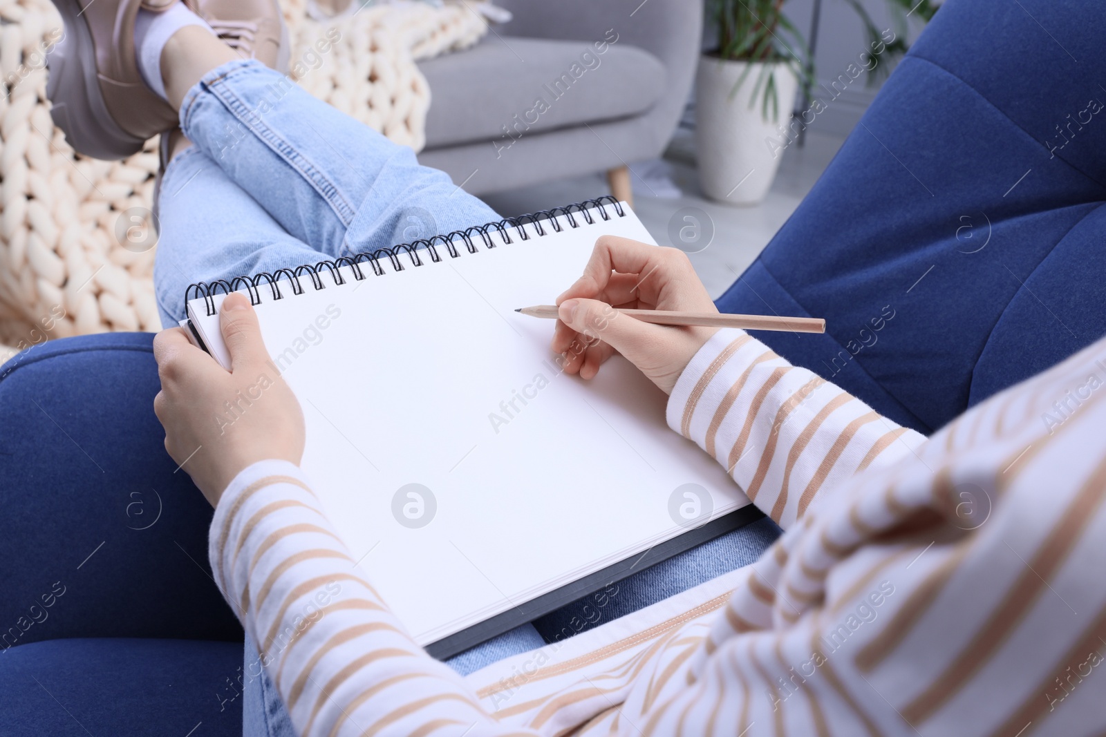 Photo of Young woman drawing in sketchbook at home, closeup