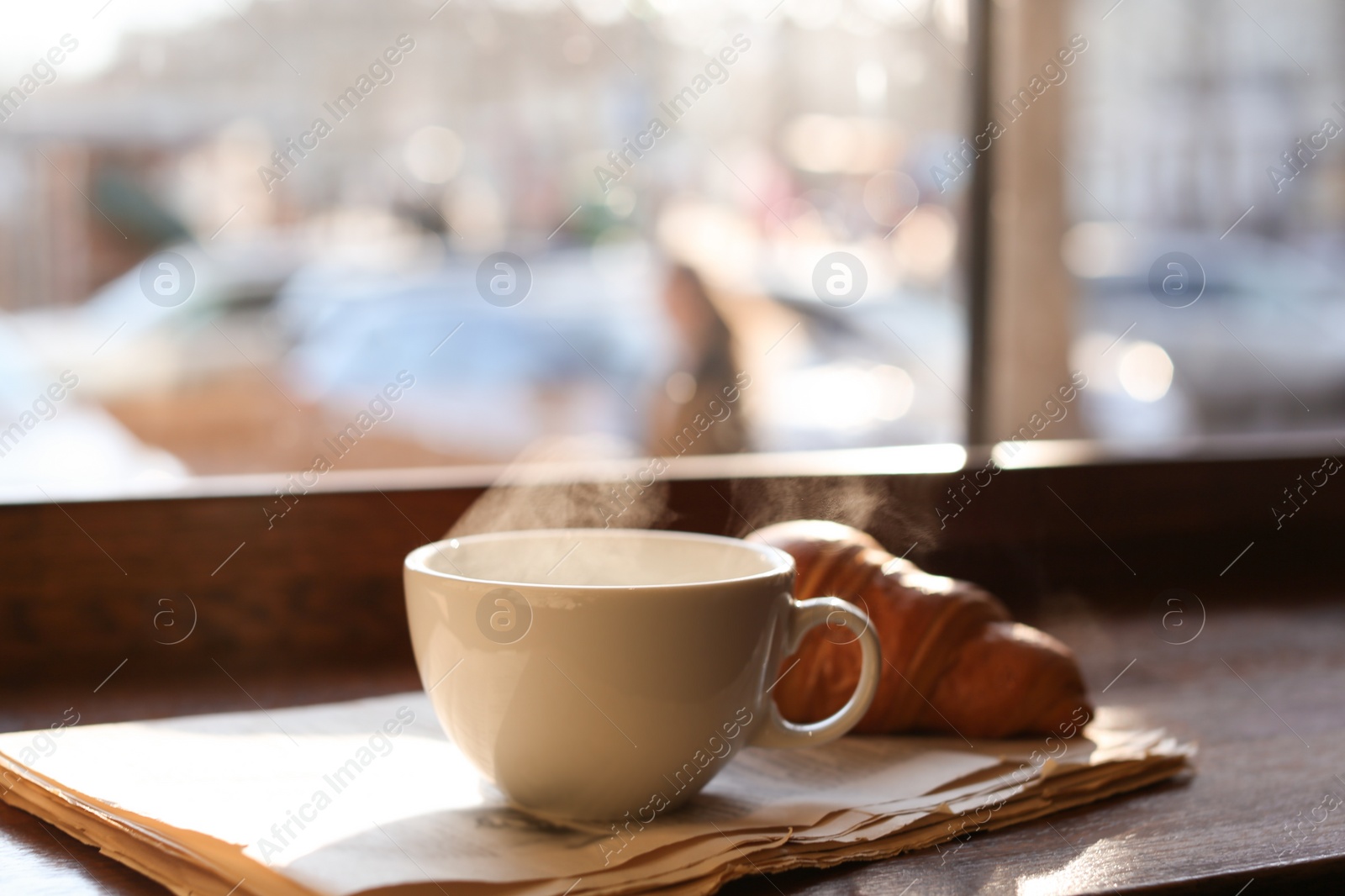 Photo of Delicious morning coffee, newspaper and croissant near window, indoors