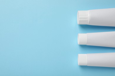 Photo of Blank tubes of toothpaste on light blue background, flat lay. Space for text