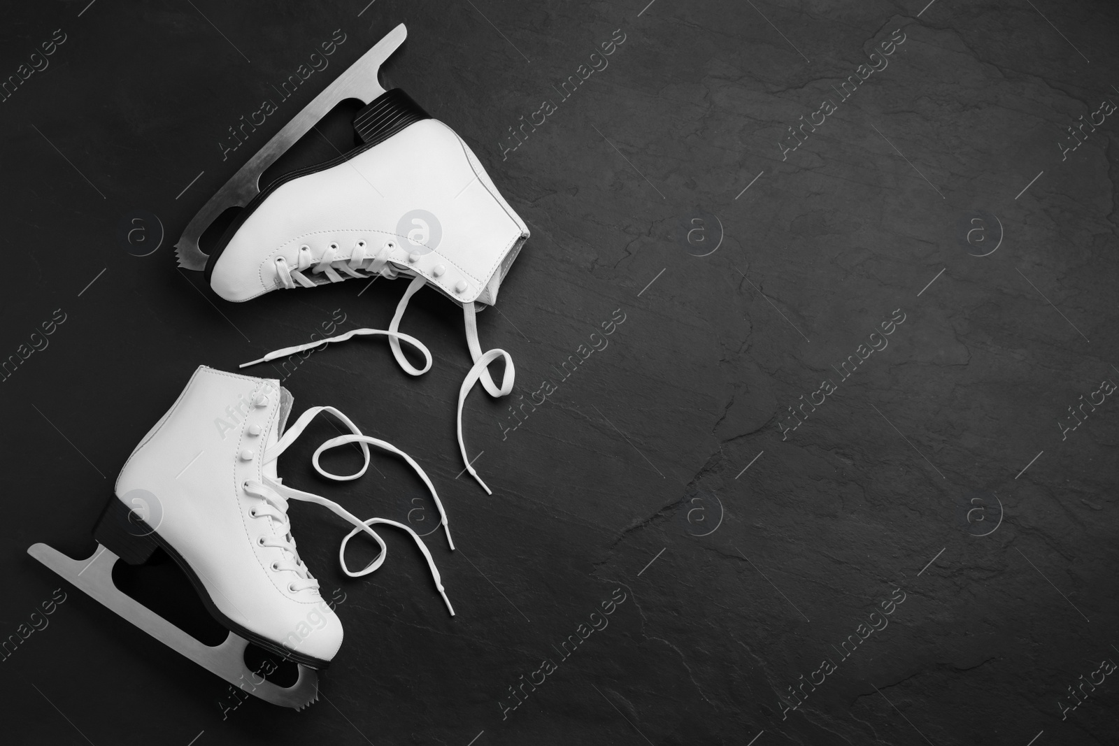 Photo of Pair of white ice skates on black stone background, top view. Space for text