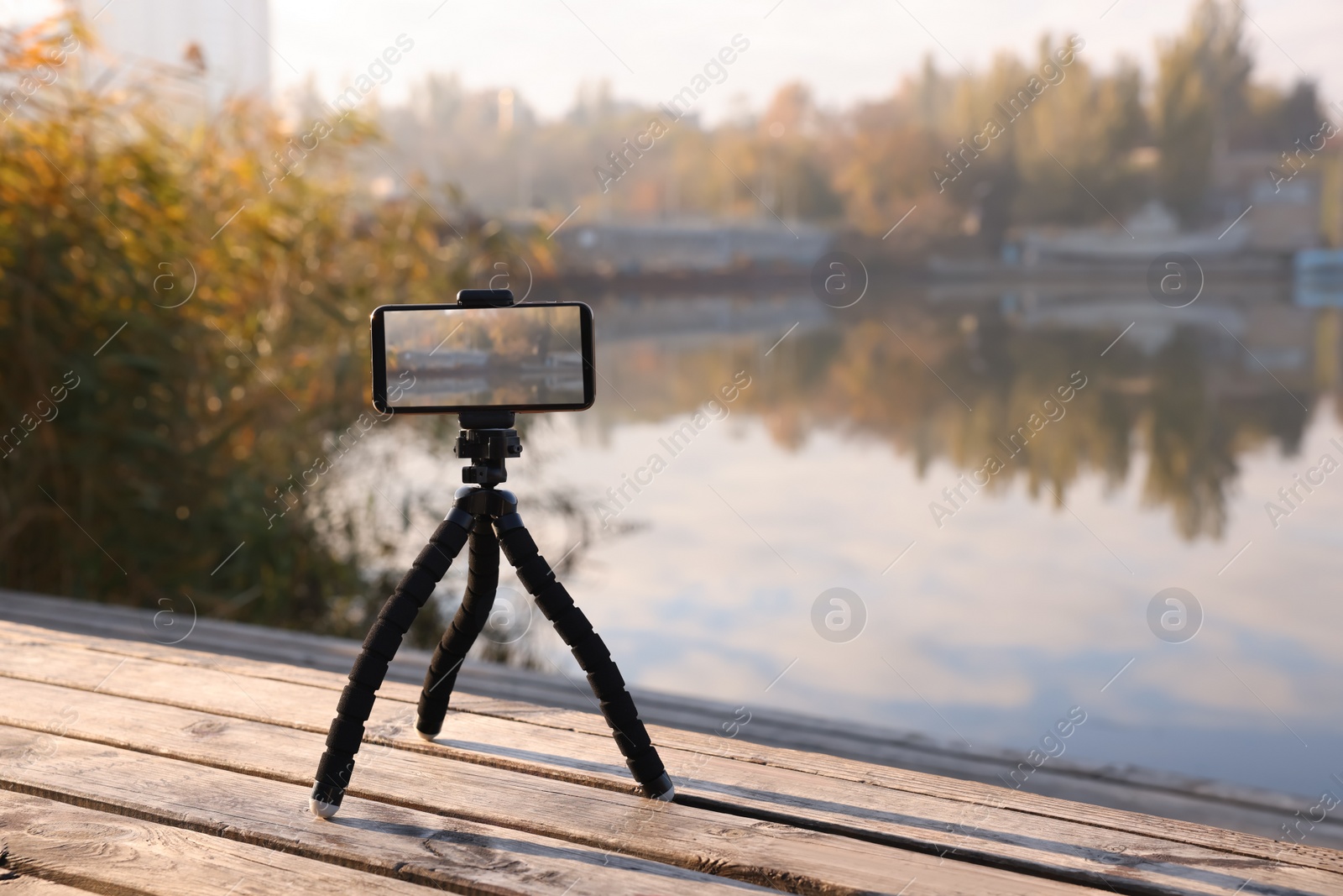 Photo of Tripod with smartphone on wooden pier near river