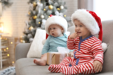 Image of Cute children in Santa hats sitting on sofa at home. Christmas celebration