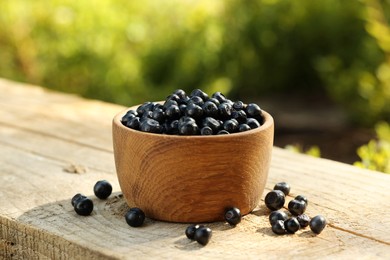 Photo of Bowl of bilberries on wooden table outdoors