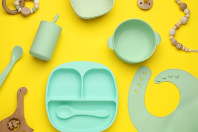Set of plastic dishware and baby accessories on yellow background, flat lay
