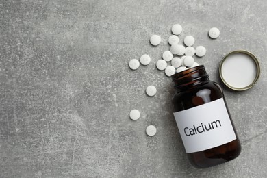 Photo of Overturned bottle of calcium supplement pills on grey table, flat lay. Space for text