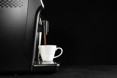 Making coffee with modern espresso machine on grey table against black background. Space for text