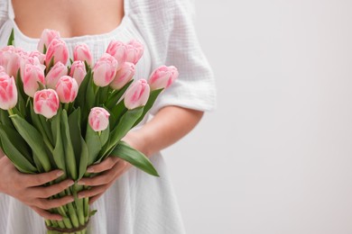 Photo of Woman with bouquet of beautiful fresh tulips on light grey background, closeup. Space for text