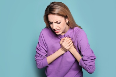 Young woman having heart attack on color background