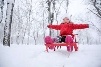 Photo of Cute little girl enjoying sleigh ride outdoors on winter day, space for text