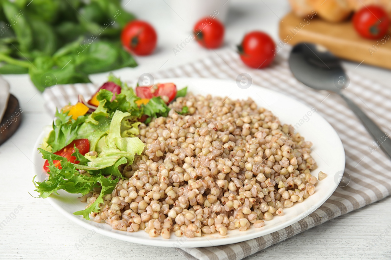 Photo of Tasty buckwheat porridge with salad on white wooden table