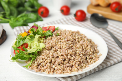 Photo of Tasty buckwheat porridge with salad on white wooden table