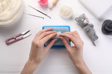 Photo of Woman felting toy from wool at white wooden table, top view