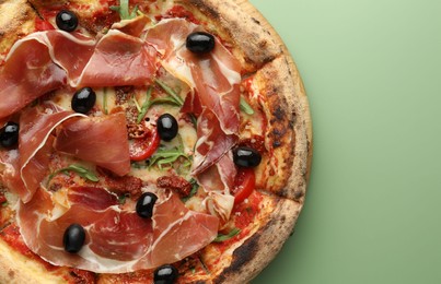 Photo of Tasty pizza with cured ham, olives and sun-dried tomato on green background, top view. Space for text