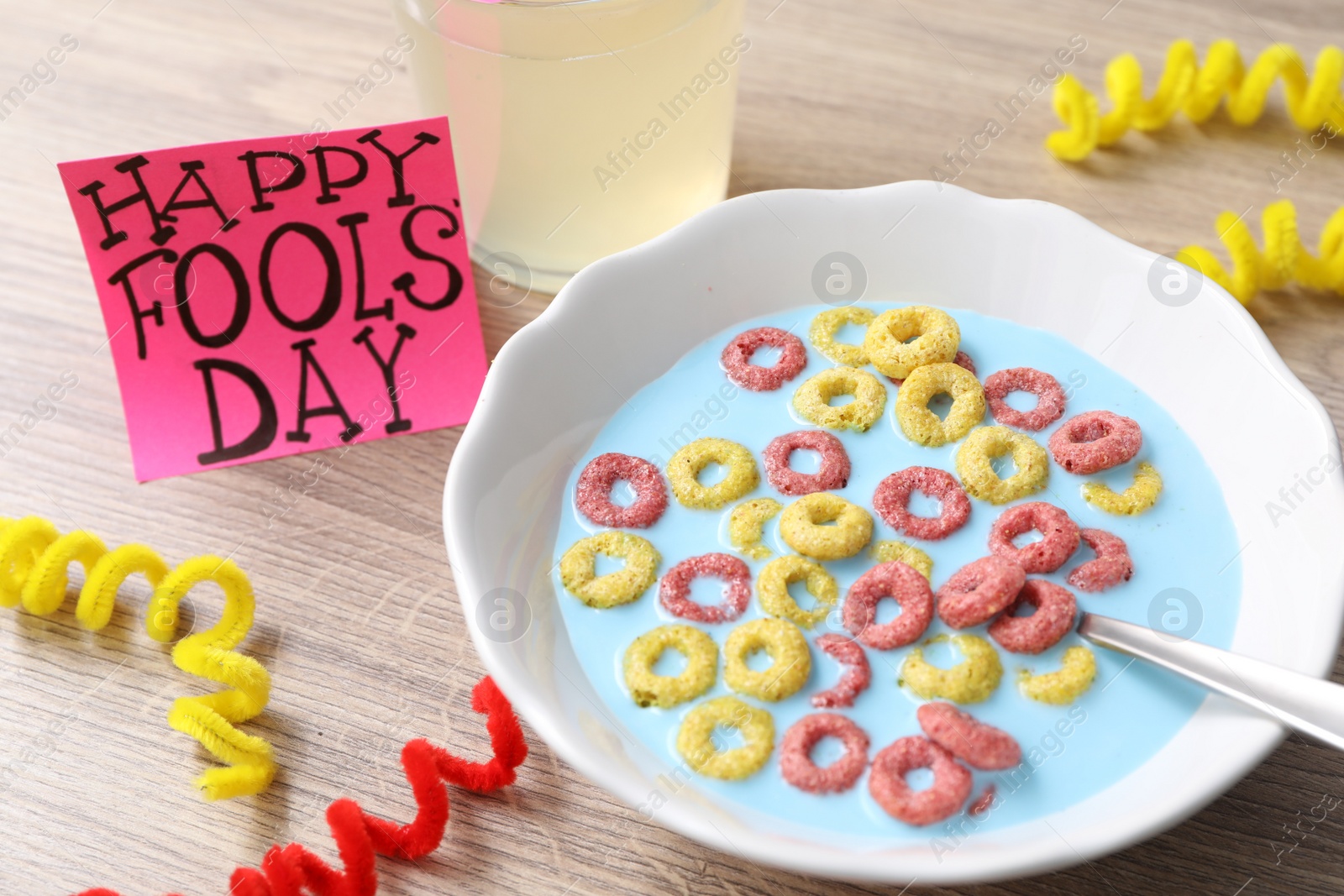 Photo of Plate of corn rings with light blue milk, drink and words Happy Fool's Day on wooden table