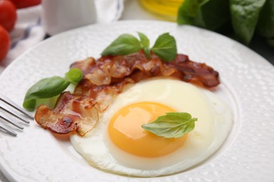 Photo of Fried egg, bacon and basil on table, closeup