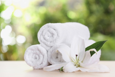 Soft bath towels and flower on table against blurred background