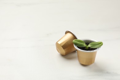 Photo of Coffee capsules and seedling on white marble table, space for text