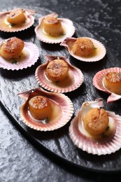 Photo of Delicious fried scallops in shells on black table, closeup