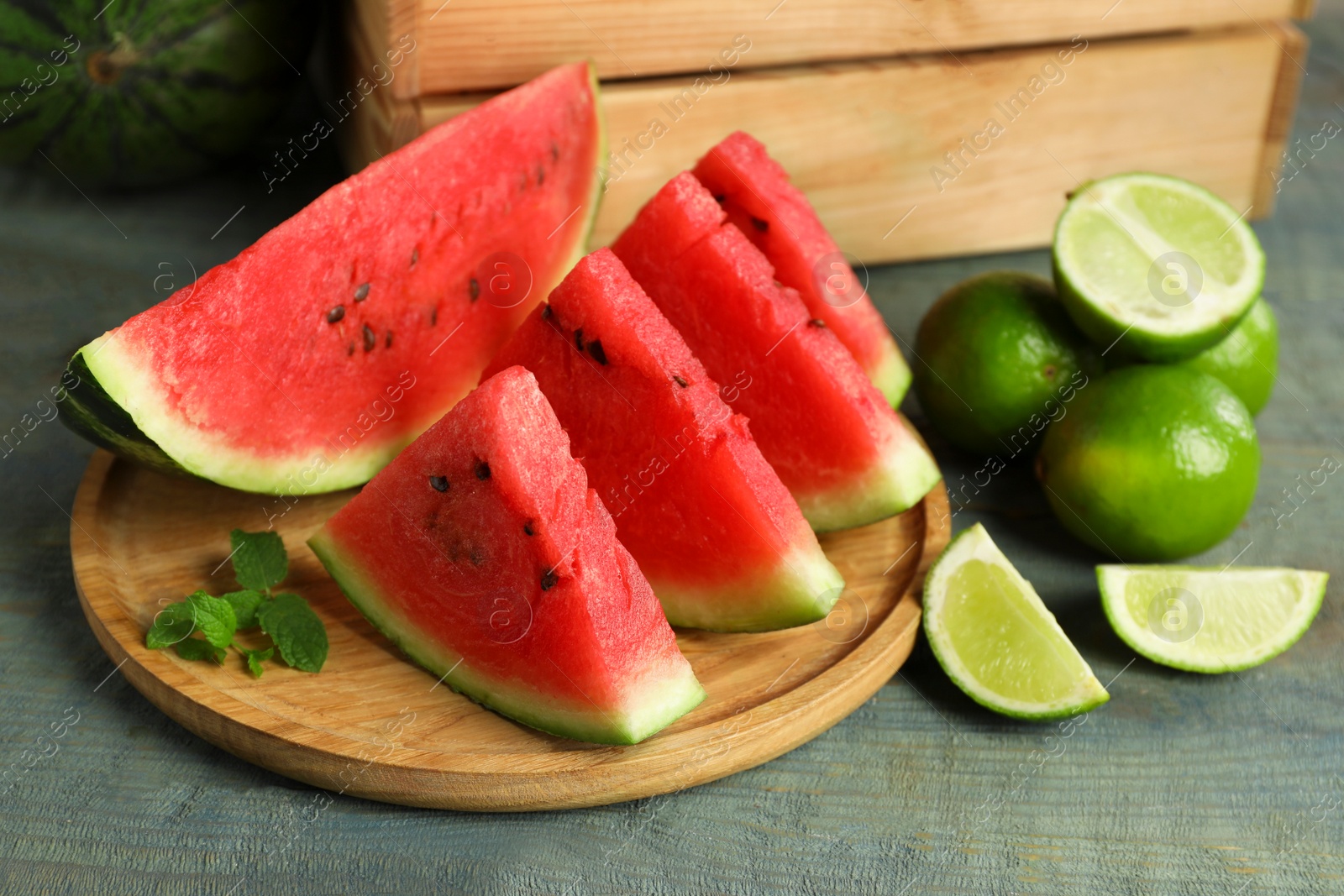 Photo of Slices of delicious watermelon, limes and mint on light blue wooden table