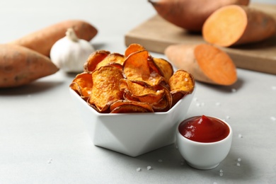 Delicious sweet potato chips in bowl and sauce on table