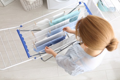 Photo of Woman hanging clean laundry on drying rack indoors, above view