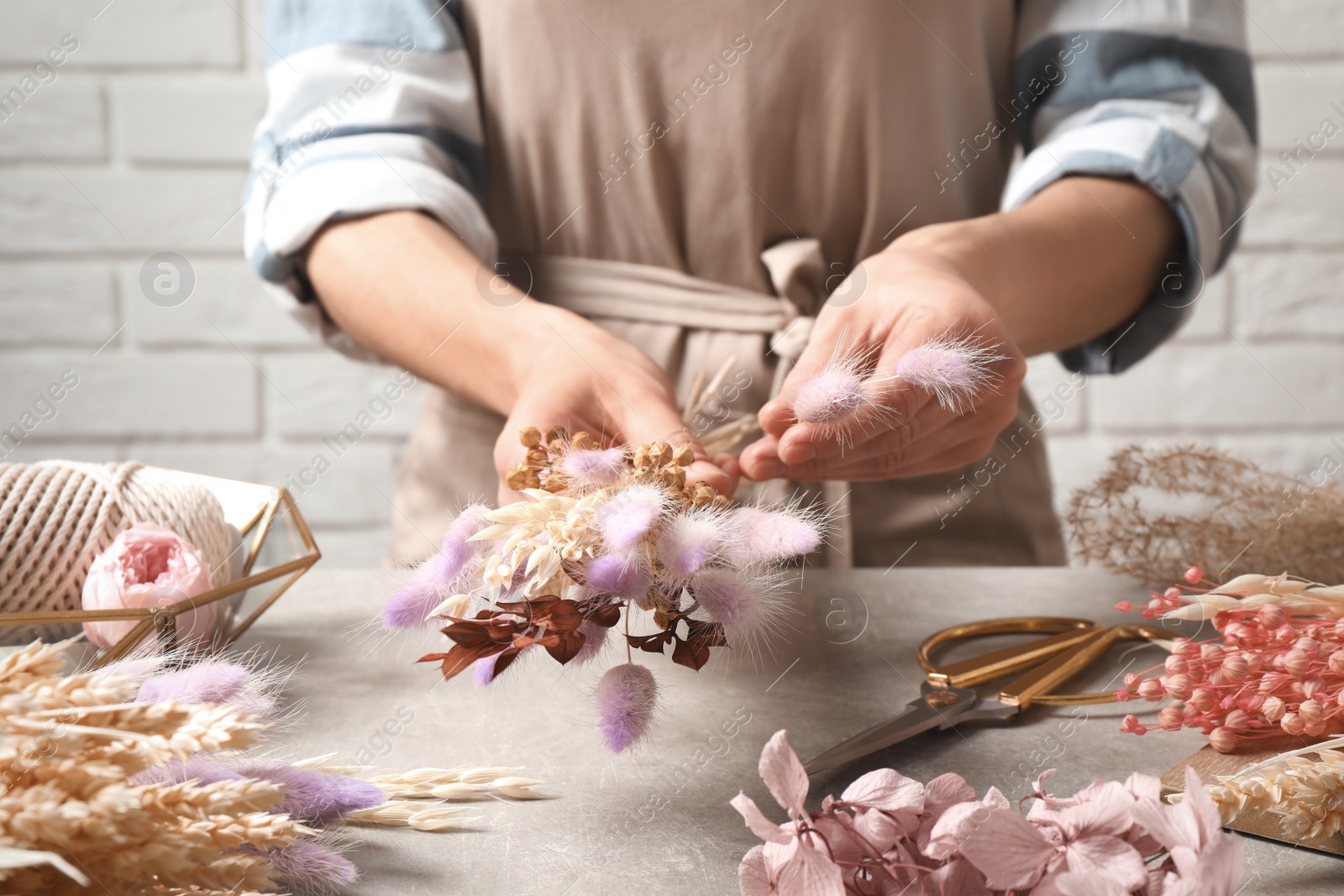 Photo of Florist making bouquet of dried flowers at grey stone table, closeup