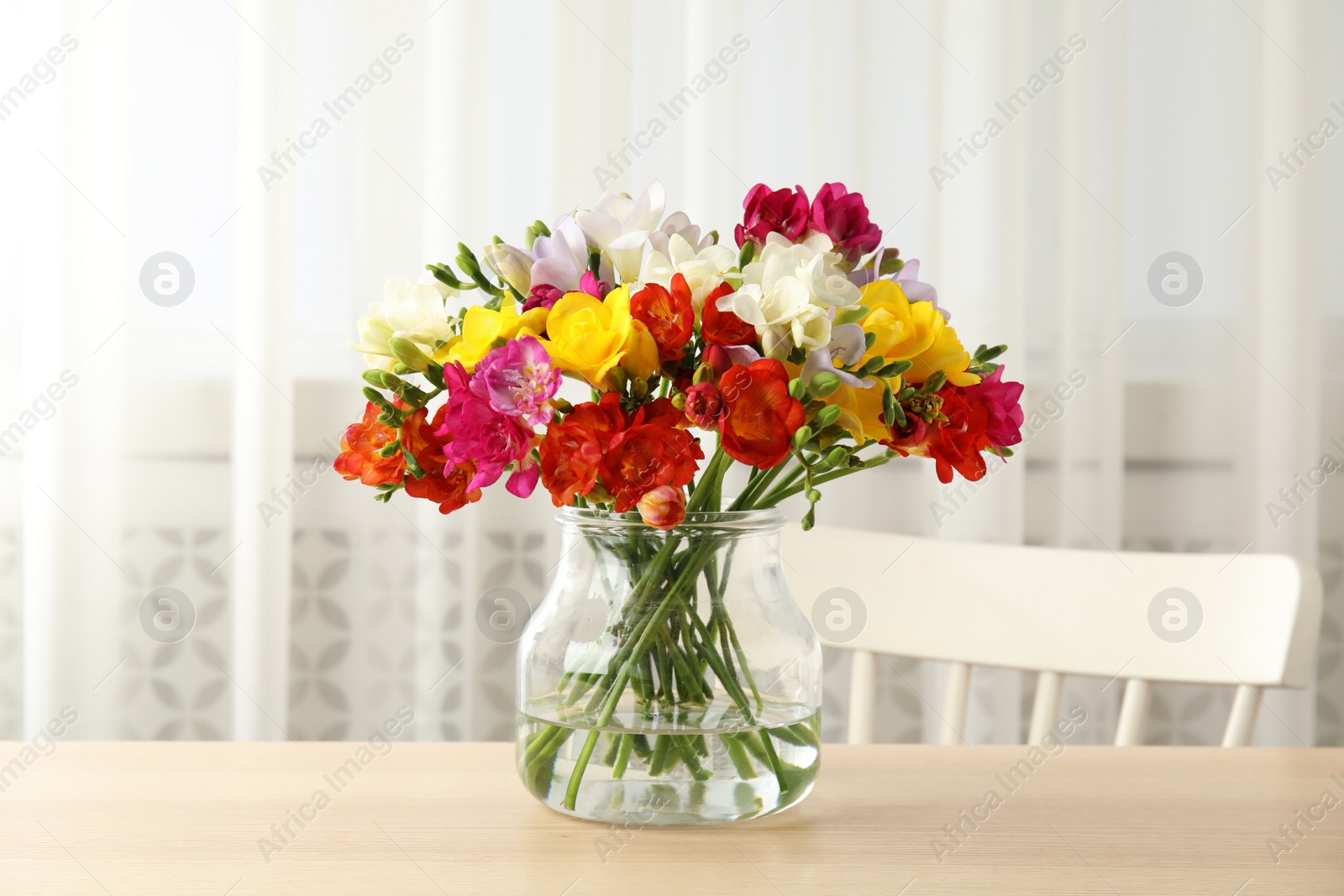 Photo of Vase with bouquet of spring freesia flowers on table in room