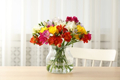 Vase with bouquet of spring freesia flowers on table in room